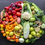 Various vegetables and fruits laid out in a circle on a dark background.